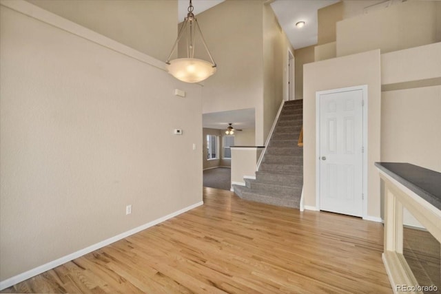 unfurnished living room featuring light wood-type flooring, stairway, baseboards, and a ceiling fan