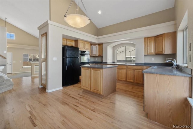 kitchen featuring dark countertops, light wood finished floors, a center island, freestanding refrigerator, and a sink