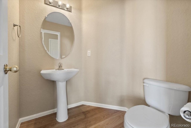 half bathroom featuring toilet, baseboards, and wood finished floors