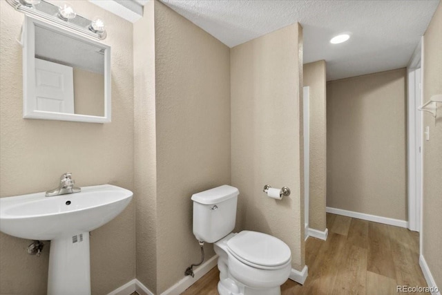 half bathroom featuring toilet, wood finished floors, and baseboards