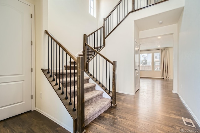 stairway with a towering ceiling, baseboards, visible vents, and wood finished floors