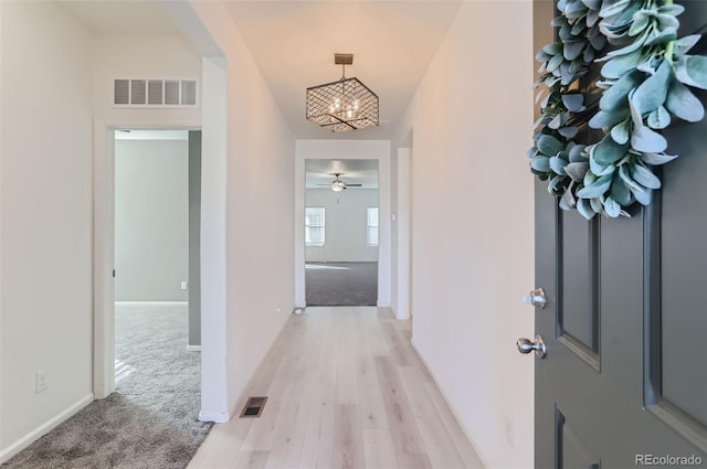 hall with light carpet and an inviting chandelier