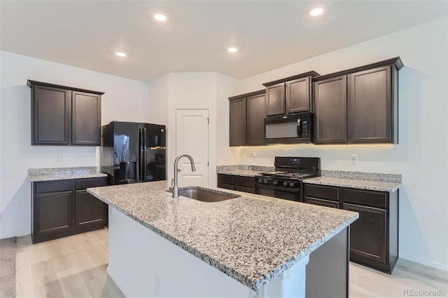 kitchen with light stone counters, sink, black appliances, and an island with sink