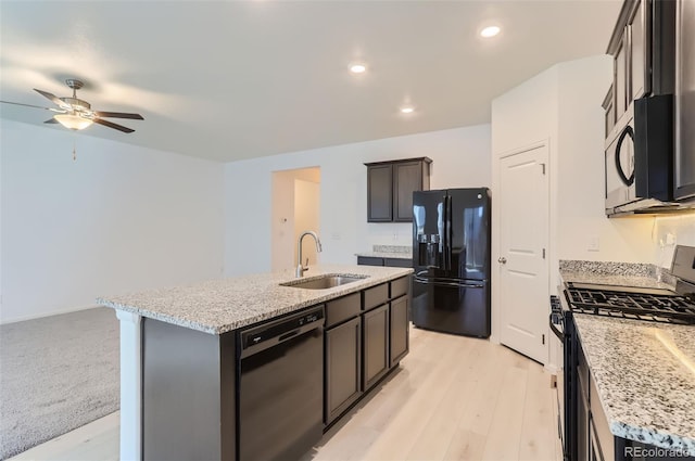 kitchen featuring light stone counters, an island with sink, sink, and black appliances