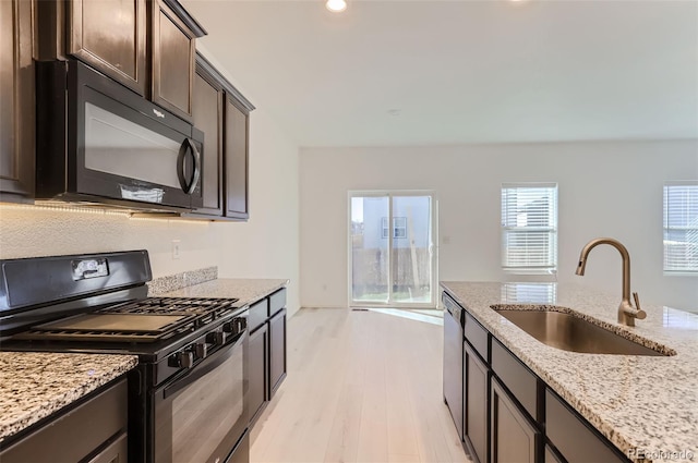 kitchen with sink, black appliances, light stone countertops, dark brown cabinets, and light wood-type flooring