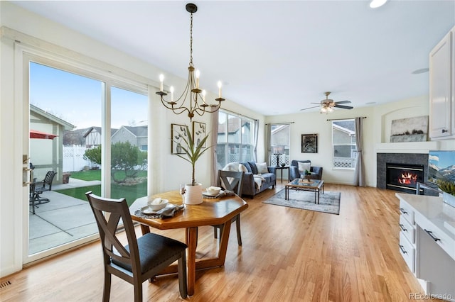 dining space with a tiled fireplace, ceiling fan with notable chandelier, and light wood finished floors