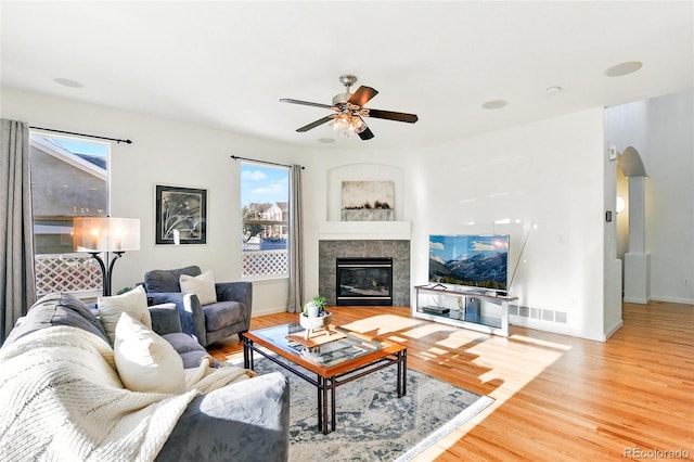 living room with a ceiling fan, wood finished floors, a healthy amount of sunlight, and a tile fireplace