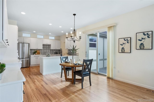 dining space featuring visible vents, an inviting chandelier, a healthy amount of sunlight, and light wood-style flooring
