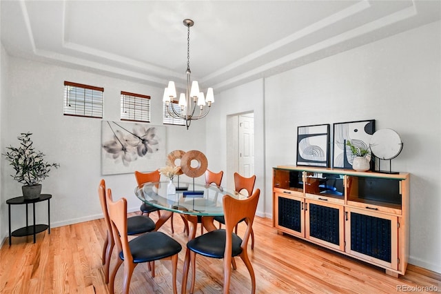 dining space with an inviting chandelier, a raised ceiling, and light wood-style floors