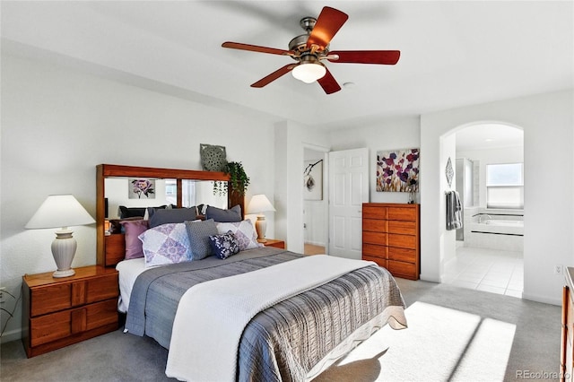 bedroom with ceiling fan, light colored carpet, arched walkways, baseboards, and connected bathroom
