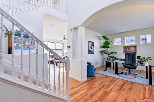 interior space featuring arched walkways, a ceiling fan, baseboards, decorative columns, and wood finished floors