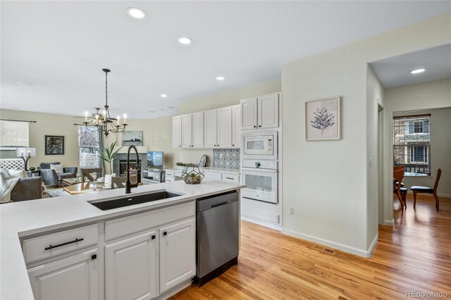 kitchen with white appliances, light countertops, white cabinets, a sink, and a notable chandelier