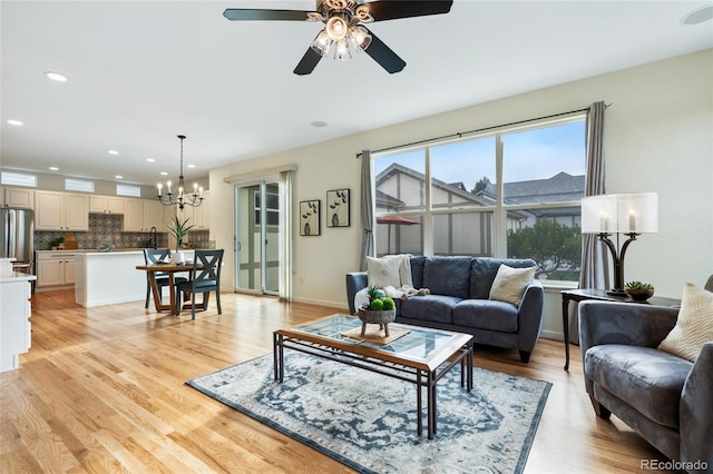 living area with recessed lighting, ceiling fan with notable chandelier, and light wood-type flooring