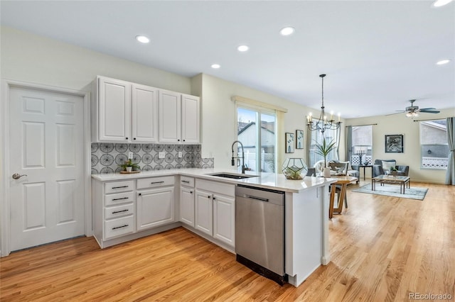 kitchen featuring stainless steel dishwasher, a sink, light wood-style floors, and a peninsula