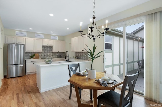 kitchen featuring a notable chandelier, a sink, freestanding refrigerator, a peninsula, and tasteful backsplash