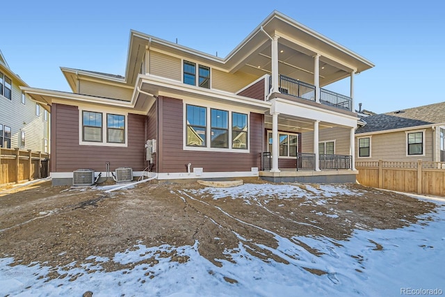 snow covered rear of property with central air condition unit, a balcony, and fence