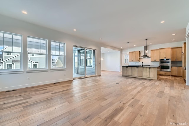 kitchen with visible vents, open floor plan, double oven, light wood-style floors, and wall chimney exhaust hood