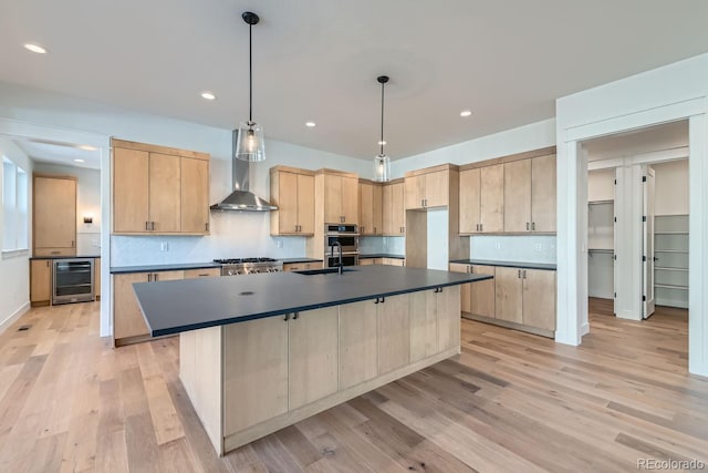 kitchen with dark countertops, wall chimney range hood, light brown cabinetry, wine cooler, and a sink