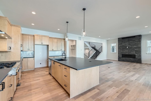 kitchen featuring dark countertops, light brown cabinetry, light wood-type flooring, stainless steel appliances, and a sink