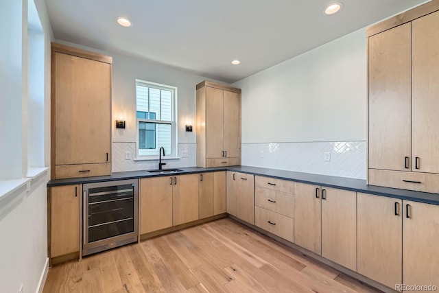 kitchen with light wood-style flooring, beverage cooler, light brown cabinets, a sink, and dark countertops