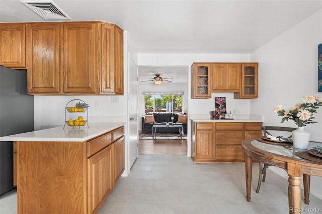 6506 Lee St, Arvada, CO 80004 - kitchen with freestanding refrigerator, brown cabinets, light countertops, glass insert cabinets, and a ceiling fan