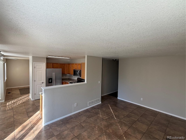 interior space featuring kitchen peninsula, dark tile patterned flooring, a textured ceiling, and appliances with stainless steel finishes