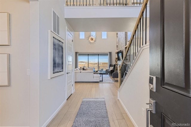 entryway featuring stairway, visible vents, baseboards, a high ceiling, and light wood-style floors