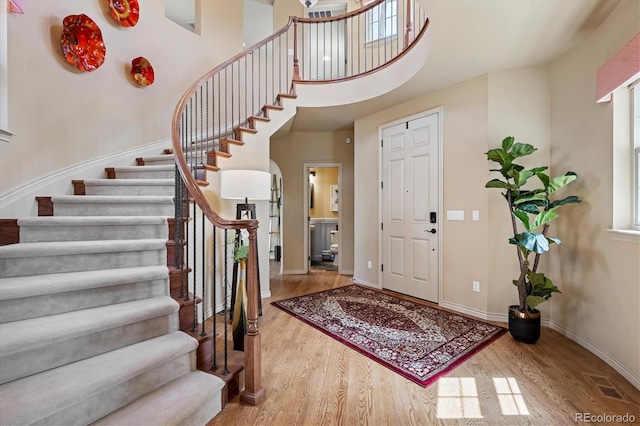 entrance foyer featuring arched walkways, stairs, baseboards, wood finished floors, and a towering ceiling