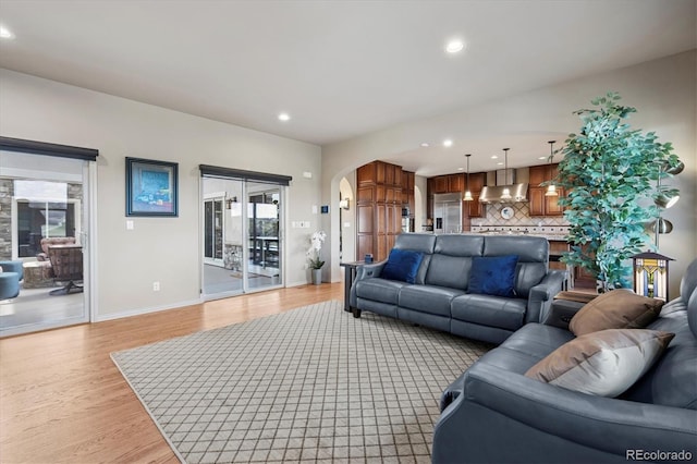 living room featuring arched walkways, recessed lighting, plenty of natural light, and light wood-style floors