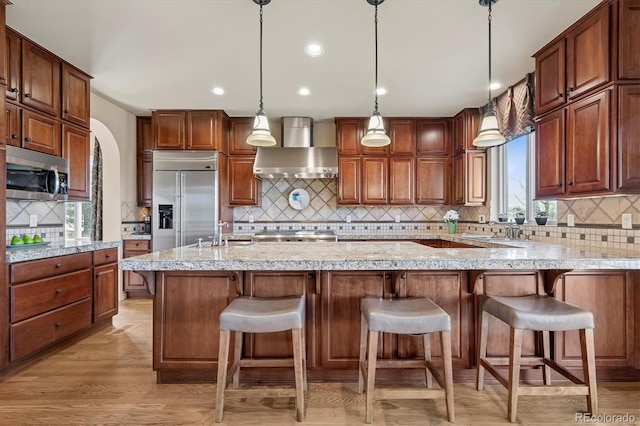 kitchen with a sink, wall chimney exhaust hood, appliances with stainless steel finishes, and backsplash