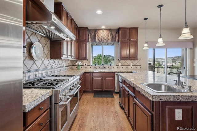 kitchen featuring wall chimney range hood, high end appliances, a center island with sink, and a sink
