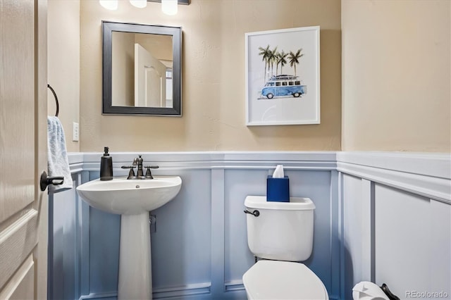 bathroom with a sink, a decorative wall, toilet, and a wainscoted wall