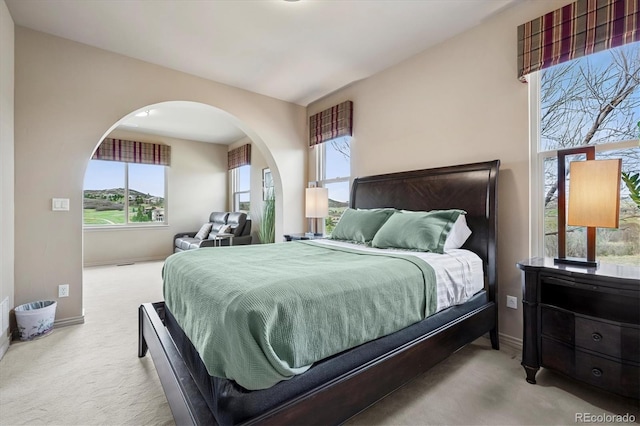 bedroom featuring carpet floors, arched walkways, baseboards, and multiple windows