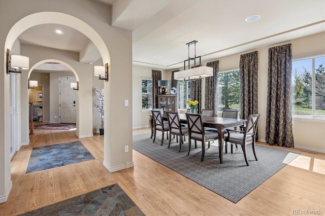 dining space featuring arched walkways, light wood-type flooring, baseboards, and recessed lighting