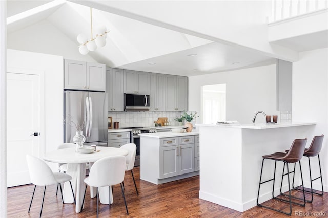 kitchen featuring gray cabinetry, vaulted ceiling, appliances with stainless steel finishes, tasteful backsplash, and kitchen peninsula