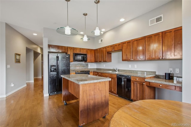 kitchen featuring light wood-style flooring, a kitchen island, a sink, black appliances, and pendant lighting