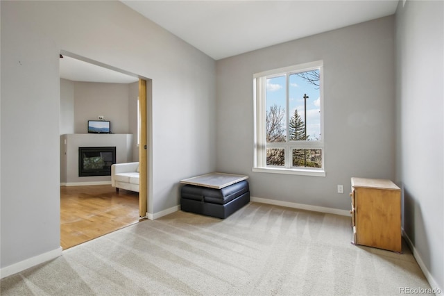 unfurnished room featuring baseboards, a glass covered fireplace, and light colored carpet