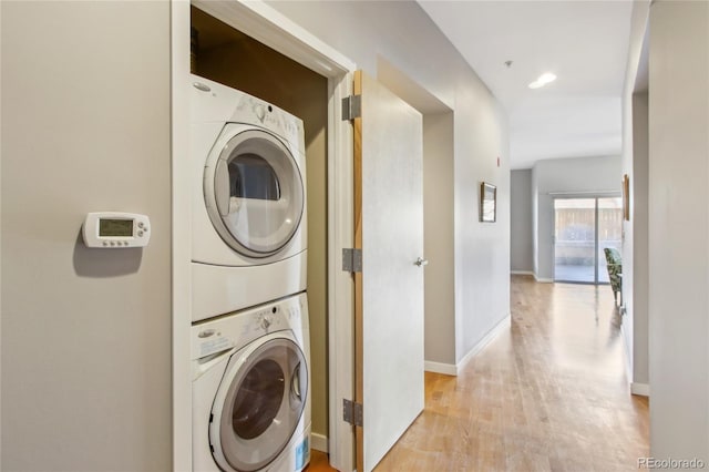 washroom with stacked washer and dryer, laundry area, light wood-style flooring, and baseboards