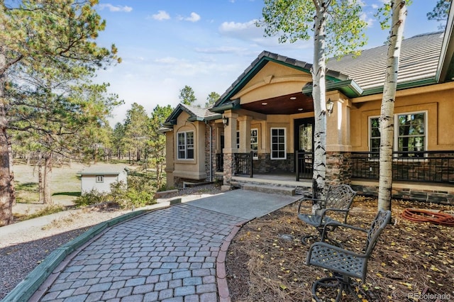 back of house featuring a porch, a tiled roof, stone siding, and stucco siding