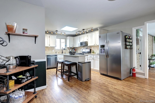 kitchen featuring a skylight, stainless steel appliances, light wood-style flooring, and white cabinets