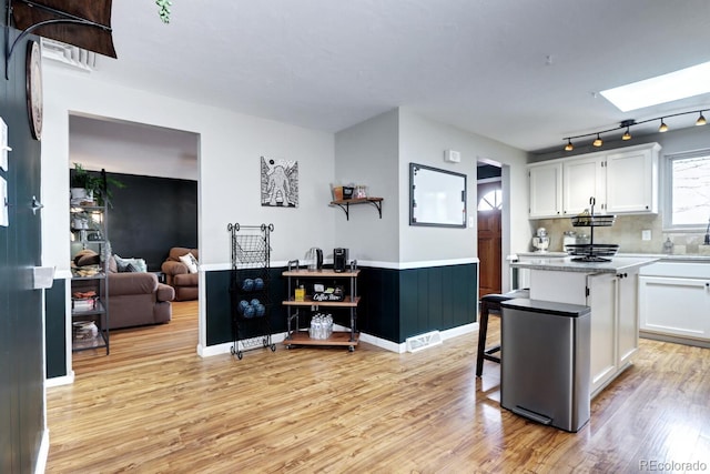 kitchen featuring white cabinets, light countertops, light wood-type flooring, and a skylight