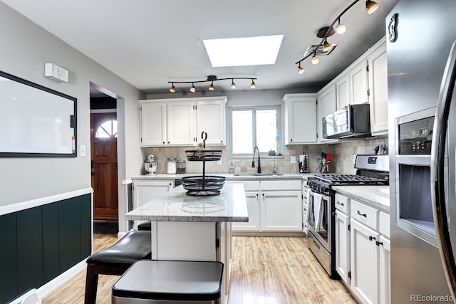 kitchen featuring white cabinets, appliances with stainless steel finishes, a skylight, and a sink