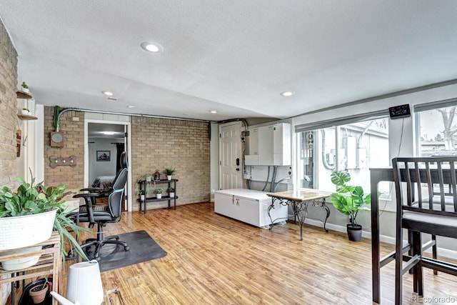 home office featuring a textured ceiling, light wood-type flooring, and brick wall