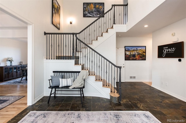 stairs featuring a high ceiling, wood finished floors, visible vents, and baseboards