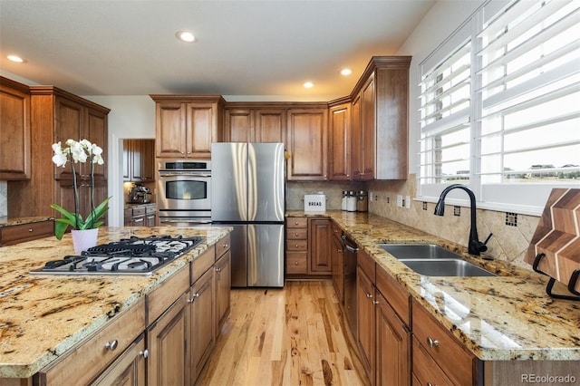 kitchen with light wood finished floors, backsplash, appliances with stainless steel finishes, a sink, and light stone countertops