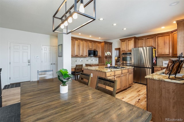 kitchen featuring tasteful backsplash, brown cabinetry, appliances with stainless steel finishes, a center island, and light stone countertops