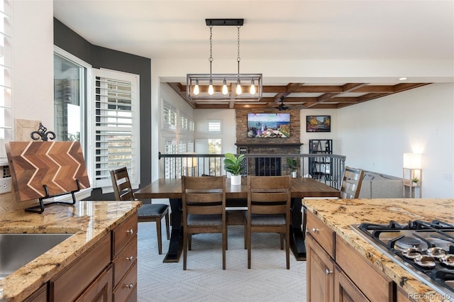 kitchen with light stone counters, beam ceiling, stainless steel gas cooktop, hanging light fixtures, and a ceiling fan