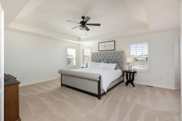 bedroom featuring light carpet, a tray ceiling, and baseboards