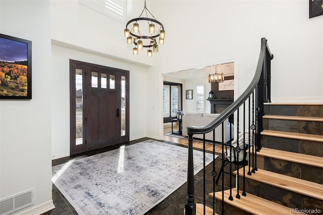 foyer entrance featuring visible vents, baseboards, a towering ceiling, stairs, and a chandelier