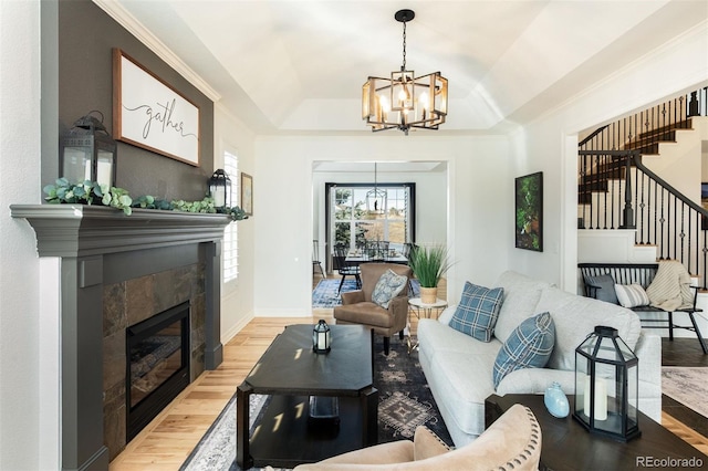 living room featuring a chandelier, a tile fireplace, wood finished floors, ornamental molding, and stairway